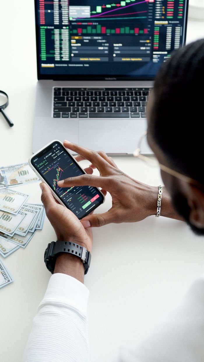 Services A person trading stocks using a smartphone, showcasing financial data on mobile and laptop screens.
